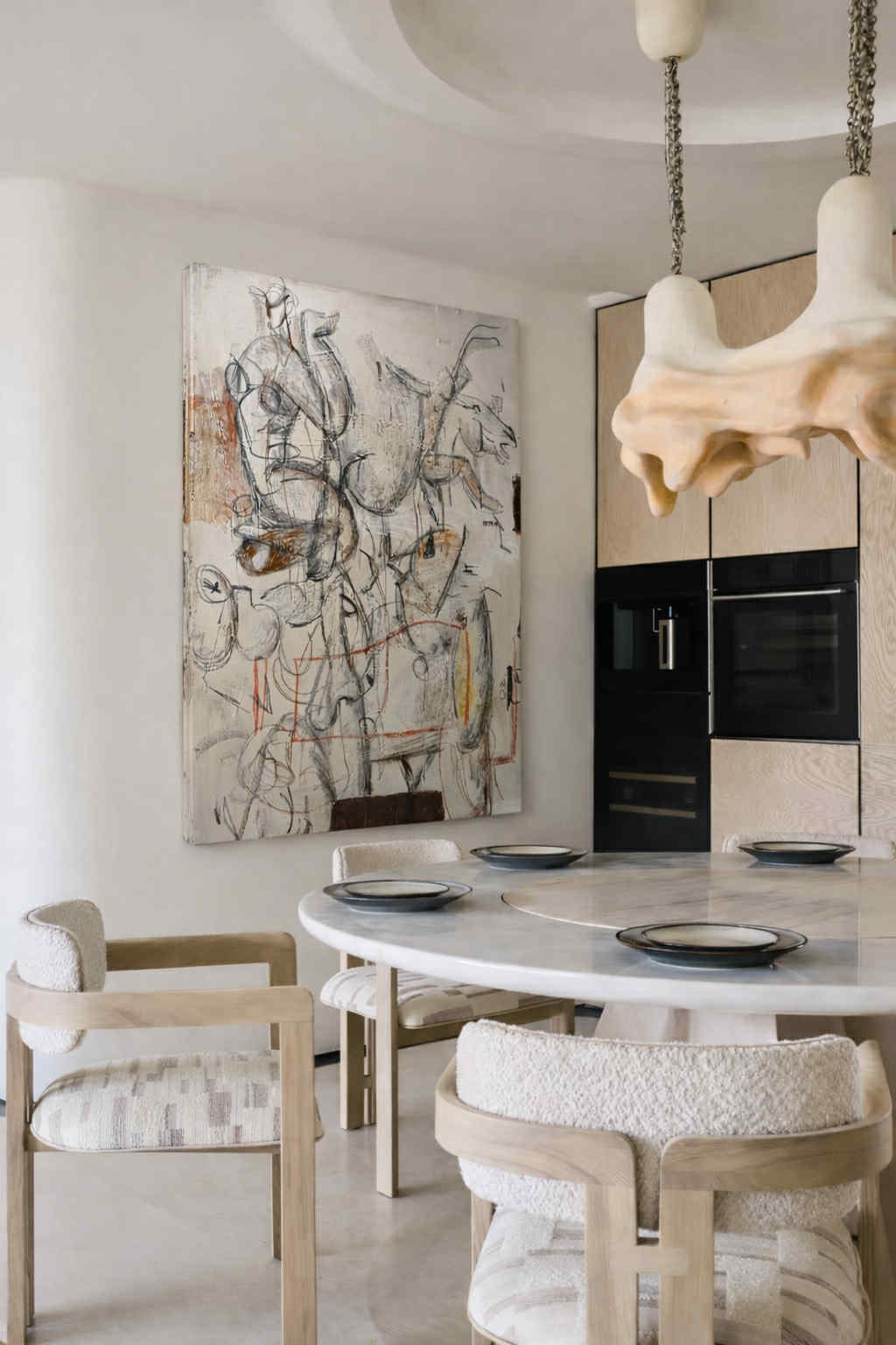 Modern kitchen with marble table and chairs, abstract art on wall, and stylish pendant lights.